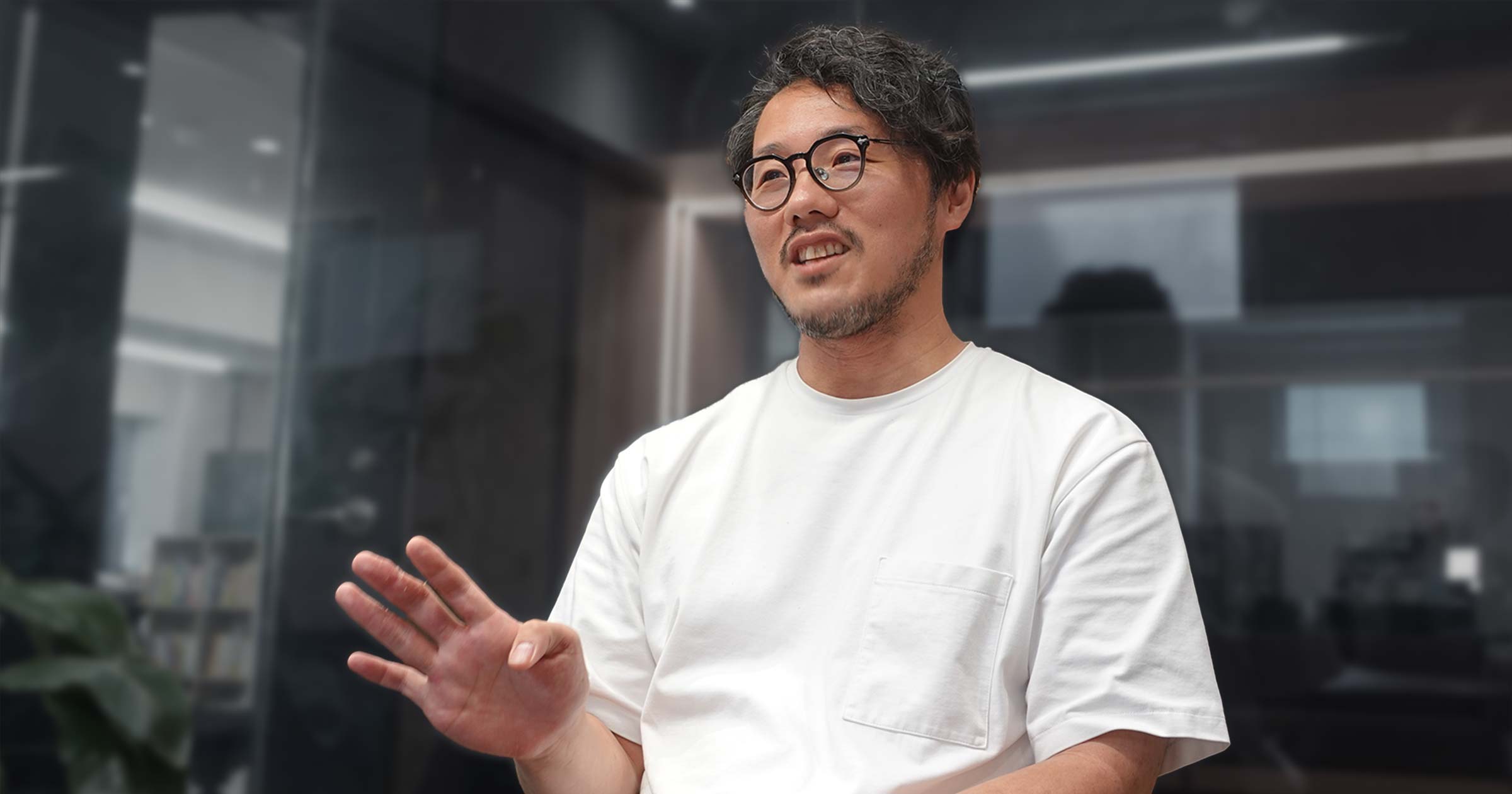 右手を挙げて話すミナベさん
